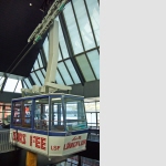La cabina della funivia a servizio pendolare Spielboden – Längfluh della S.A. della teleferiche Saas Fee (LSF), anno d’inaugurazione 1984La più moderna funivia a servizio pendolare con grandi cabineQuesta funivia a servizio pendolare, costruita secondo i più moderni criteri di sicurezza, possiede un meccanismo di scorrimento con 18 rotelle a due cavi con un sistema di freni separatamente attaccato. La forma esteriore delle cabine per i passeggeri venne cosi ideata, affinché essa possa garantire ai passeggeri il suo miglior comportamento possibile in caso di forte vento, offrendo nello stesso tempo una bella vista panoramica con le sue grandi finestre. La necessaria stabilità viene tra l’altro raggiunta mediante una speciale costruzione del fondo. Per garantire la sicurezza, accanto ai dispositivi nella stazione, c’è anche nella cabina un congegno, che serve per misurare il peso del carico con le indicazioni in cristallo fuso. In caso di sovraccarico si sente un segnale d’allarme e nello stesso tempo la cabina si blocca elettricamente. L’apparecchio è montato fisso su un quadro di manovra, che serva alla guida teleferica e dove si possono controllare i dati importanti. Mediante un citofono si può mantenere il contatto non solo con le altre cabine, ma anche con la stazione. Tirando una maniglia d’emergenza posta al di sopra del quadro si può azionare il freno di bloccaggio. Un boccaporto apribile nel pavimento della cabina, dal quale si può far passare un congegno con una corda e un sacco, serve par salvare i passeggeri e farli uscire dalla cabina bloccata.
